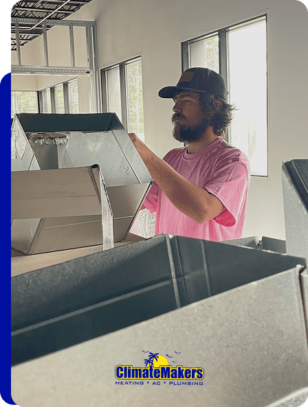 A man in a pink shirt and cap works with metal HVAC duct components inside a building, representing the expertise of ClimateMakers. The ClimateMakers Heating, AC, Plumbing logo is visible at the bottom of the image.