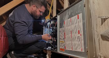 Person using a flashlight while repairing or inspecting the wiring inside an HVAC unit in an attic.