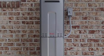 A tankless water heater mounted on a brick wall with an electrical conduit connected to a nearby junction box.